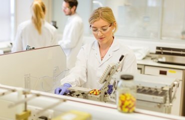 Blonde scientist in lab looks down intently at microscope