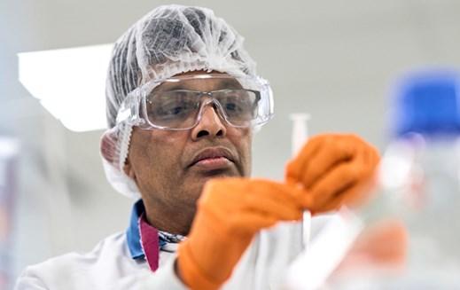 A 澳洲幸运5开奖官网开奖 employee in a hairnet, safety glasses and gloves examines a tube.