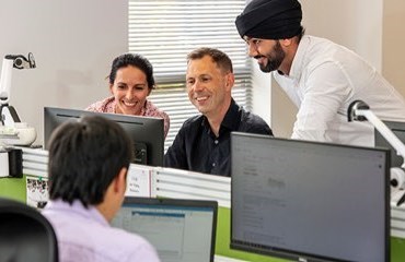 Two people sitting looking at a computer screen and another person standing looking at the screen