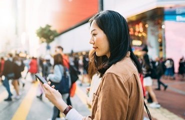 Busy street crossing person with beige jacket looks at their phone 