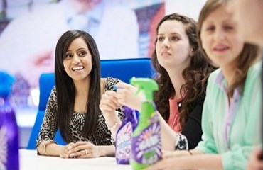 Cillit Bang employees sit around a table with purple and green bottles of Cillit Bang on it