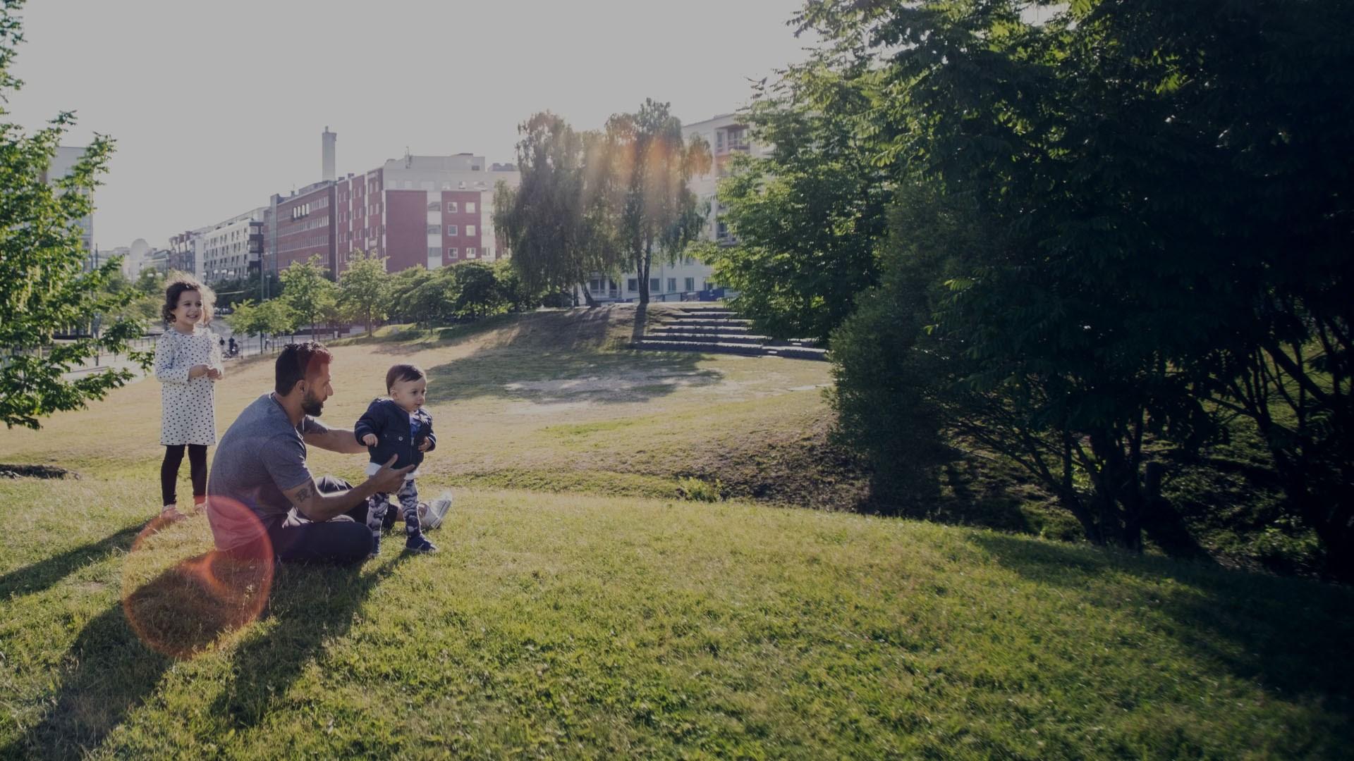Father playing with children on grassy field at park against sky.
