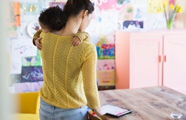 Parent standing up holding a baby looking at an iPad in a nursery