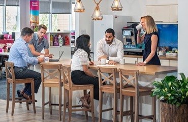 Colleagues sitting and standing around a table in an office kitchen