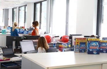 Person sitting in an office facing a computer with three different boxes of Finish on the cupboard behind her