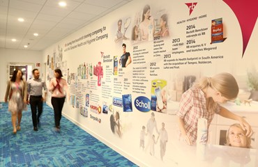 Three colleagues walk down corridor in the RB office with a company timeline on the wall