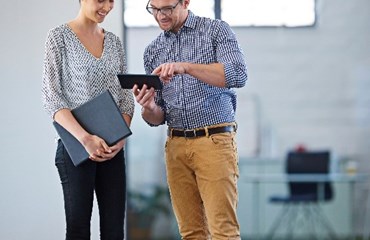 Two people stand together in room looking at a tablet device