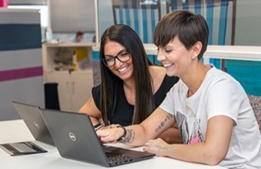 Two employees sitting in front of laptops pointing at the screen