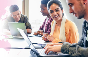 Diverse group of young adults sitting around table working on laptops